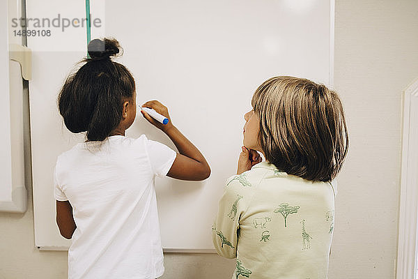 Junge betrachtet Schulmädchen beim Schreiben an der Tafel in der Grundschule