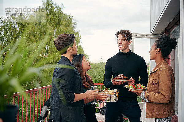 Junger Mann unterhält sich mit Freunden beim Essen während einer Party auf der Terrasse