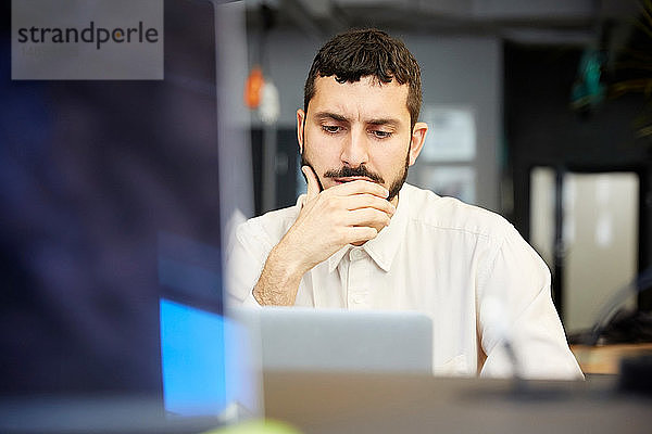 Gestresster kreativer Geschäftsmann schaut auf Laptop  während er im Büro sitzt