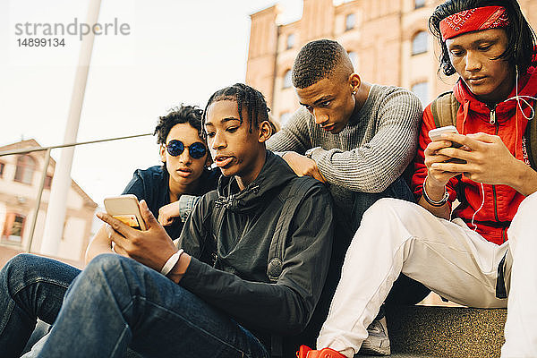 Männliche Freunde benutzen Mobiltelefone  während sie in der Stadt sitzen