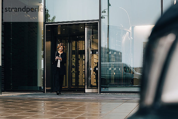 Geschäftsfrau in voller Länge mit Smartphone beim Verlassen des Büros