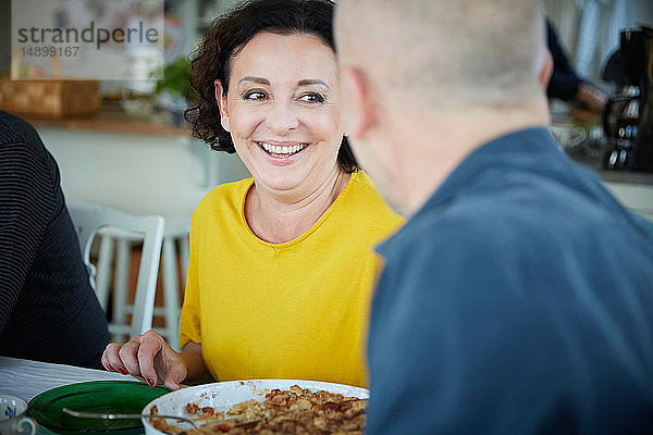 Fröhliche reife Frau unterhält sich mit einem männlichen Freund beim Mittagessen zu Hause