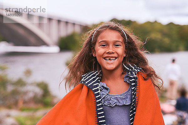 Porträt eines fröhlichen Mädchens mit orangefarbener Decke  das während des Picknicks im Park steht