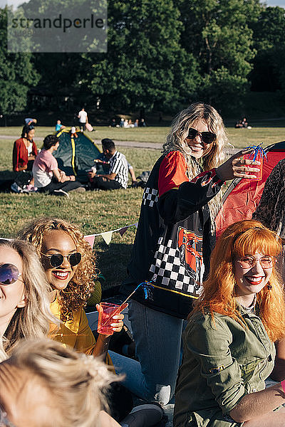 Lächelnde Freunde  die am sonnigen Tag beim Zelten einen Drink genießen  im Konzert