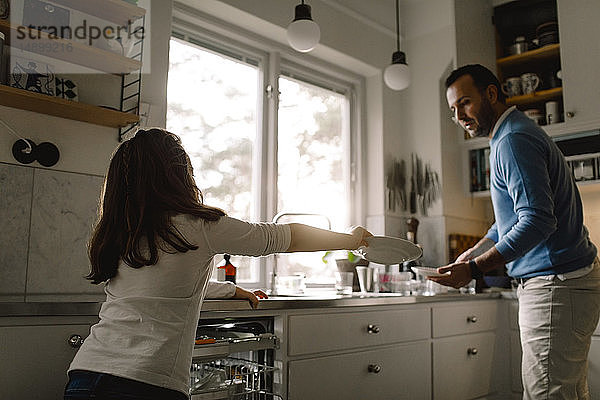 Tochter gibt dem Vater einen Teller  während sie zu Hause in der Küche steht