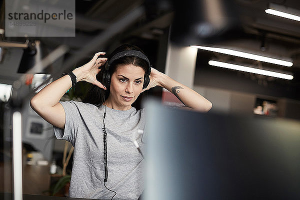 Kreative Geschäftsfrau trägt Kopfhörer  während sie im Büro auf den Computermonitor schaut