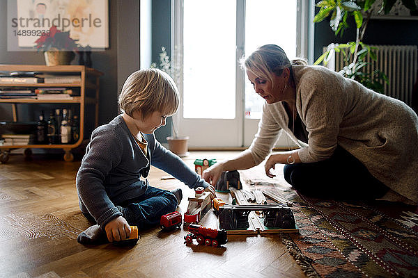 Mutter und Tochter spielen mit der Spielzeugeisenbahn  während sie im Wohnzimmer auf dem Hartholzboden sitzen
