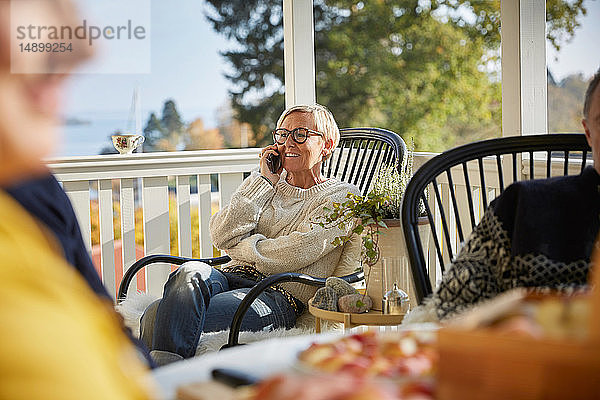 Lächelnde reife Frau  die auf der Veranda sitzend ein Smartphone beantwortet