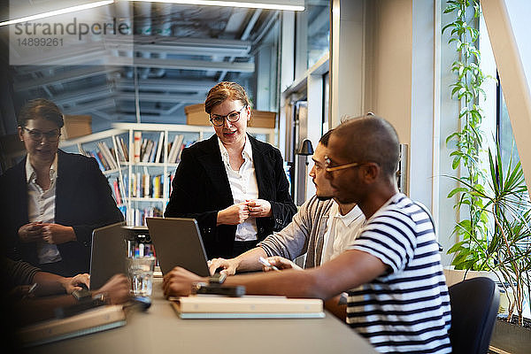 Männliche Unternehmer halten eine Präsentation vor einer Bankmanagerin über einen Laptop am Schreibtisch im Kreativbüro