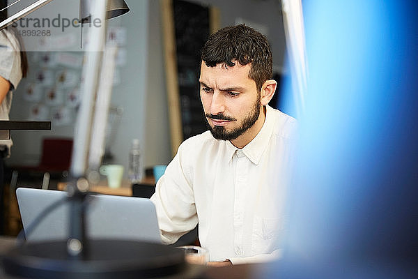 Gestresster Geschäftsmann schaut auf Laptop  während er im Kreativbüro sitzt