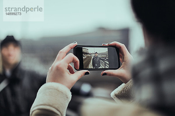 Ausgeschnittenes Bild einer Frau  die einen Freund mit einem Smartphone auf der Straße in der Stadt fotografiert