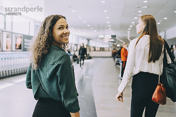 Porträt einer lächelnden Geschäftsfrau  die mit einer Kollegin am Flughafen spazieren geht