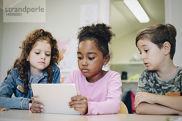 Schulfreunde lernen durch digitales Tablet am Schreibtisch im Klassenzimmer