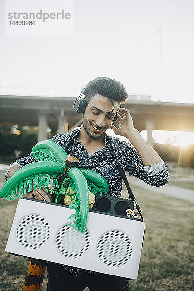 Lächelnder junger Mann mit Lautsprecher und Palmenballon genießt Musik im Festival