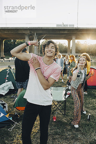 Porträt eines lächelnden Mannes  der seine Muskeln spielen lässt  während er mit Freunden beim Musikfestival genießt