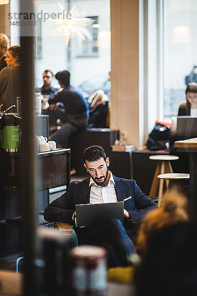Selbstbewusster Geschäftsmann sitzt im Kreativbüro mit Laptop auf einem Stuhl