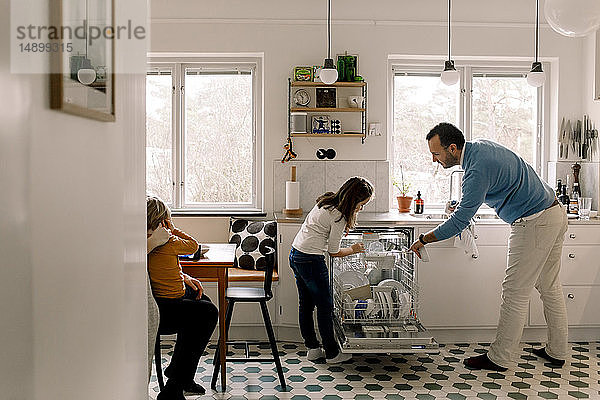 Vater und Tochter ordnen Utensilien in der Geschirrspülmaschine an  während sie in der Küche stehen