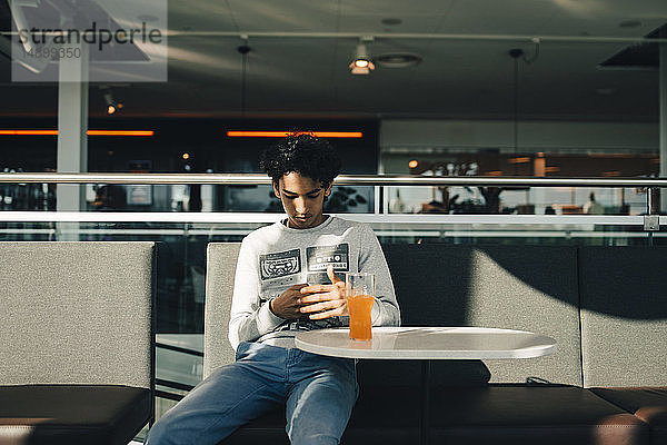 Teenager-Junge benutzt Mobiltelefon  während er im Restaurant sitzt