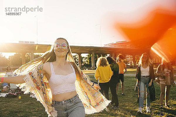 Lächelnde Frau tanzt mit Freunden im Hintergrund bei einer Veranstaltung an einem sonnigen Tag