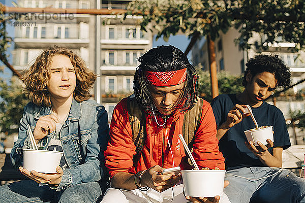 Junger Mann benutzt Mobiltelefon  während Freunde in der Stadt an einem sonnigen Tag essen gehen