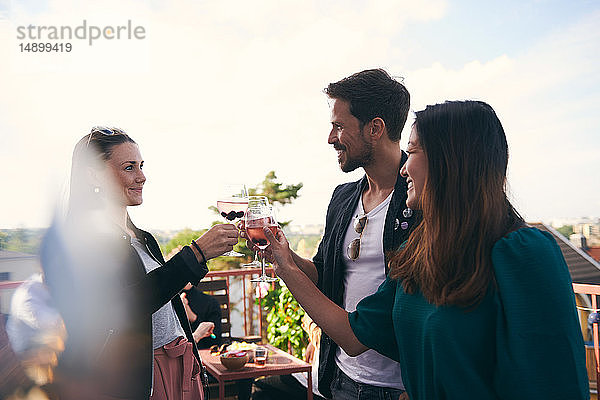 Lächelnde Freunde stoßen bei einer Party auf der Terrasse auf Getränke an