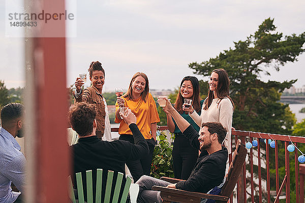 Glückliche Freunde stoßen während der Party auf der Terrasse auf Getränke an