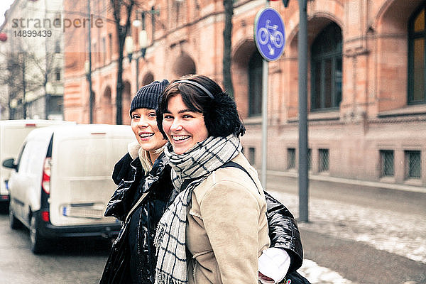 Porträt fröhlicher junger Frauen in warmer Kleidung  die im Winter in der Stadt auf der Straße stehen