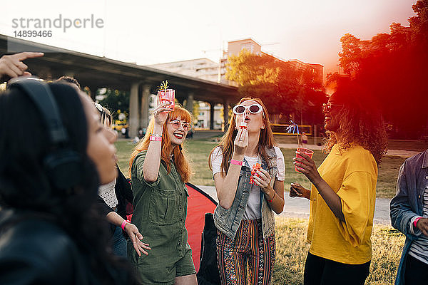 Freunde genießen im Sommer während des Musikfestivals Getränke und blasen Seifenblasen