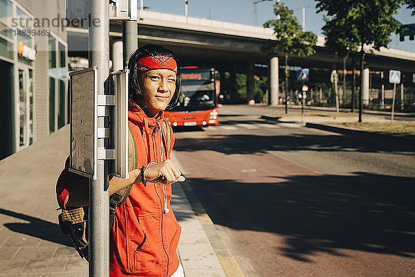 Porträt eines lächelnden jungen Mannes  der zwinkernd an der Bushaltestelle steht  während eines sonnigen Tages