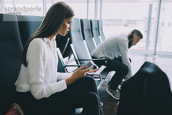 Junge Geschäftsfrau mit Smartphone und Reisepass im Wartebereich des Flughafens
