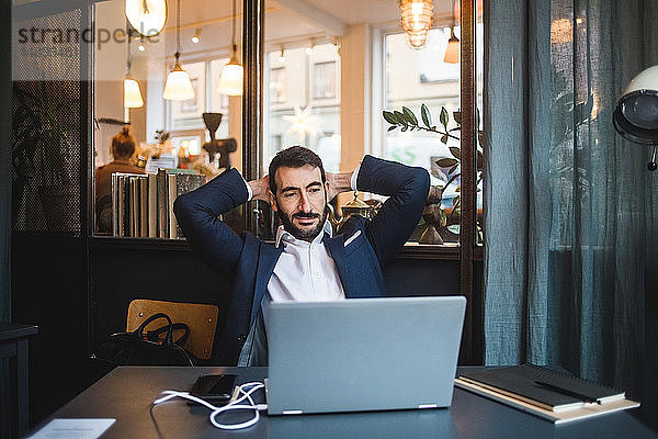 Geschäftsmann mit Händen hinter dem Kopf und Blick auf Laptop auf dem Schreibtisch im Kreativbüro