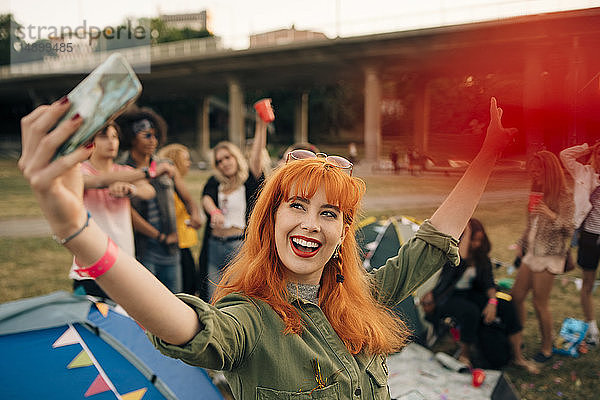 Fröhliche junge Frau  die während eines Musikfestivals mit Freunden beim Zelten Selbsthilfe betreibt