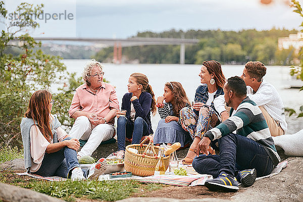 Familie und Freunde betrachten ältere Frau  während sie am Seeufer im Park sitzen