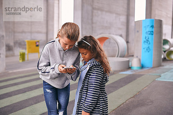 Schwestern benutzen Mobiltelefon  während sie auf dem Fußweg auf dem Spielplatz stehen