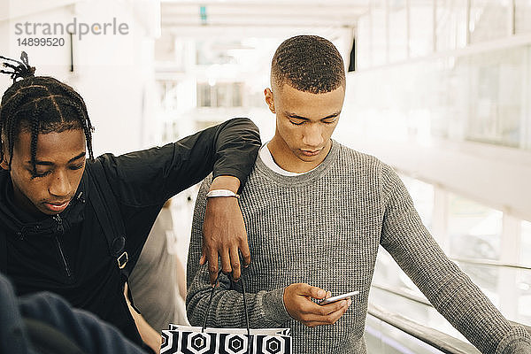 Teenager  der ein Mobiltelefon benutzt  während er einem Freund im Einkaufszentrum zur Seite steht