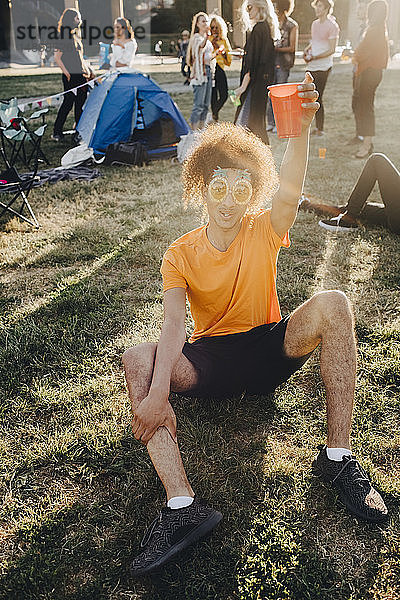 Porträt eines Mannes  der während eines Musikfestivals im Gras sitzend trinkt