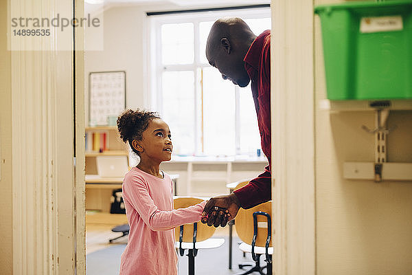 Lehrer schüttelt einem Jungen am Eingang im Klassenzimmer die Hand