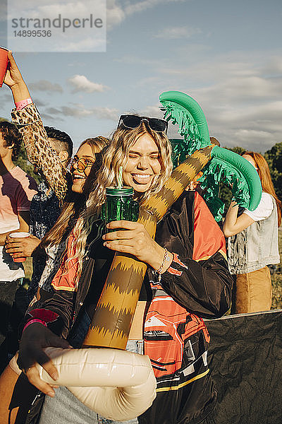 Glückliche Frau hält Ballon in der Hand  während sie mit Freunden beim Musikfestival einen Drink genießt