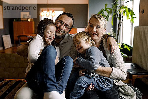 Porträt von Eltern mit fröhlichen Töchtern  die zu Hause im Wohnzimmer sitzen