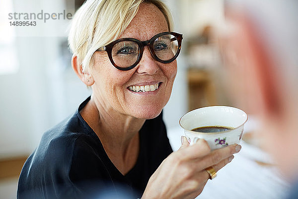Lächelnde reife Frau hält Kaffeetasse in der Hand  während sie zu Hause wegschaut