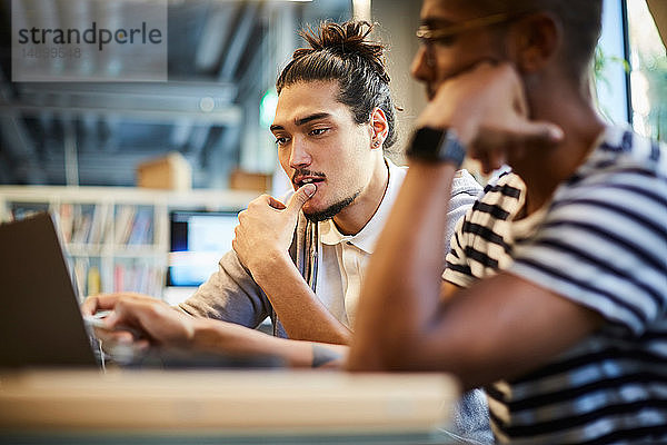 Männliche Unternehmer diskutieren über Laptop am Schreibtisch im Kreativbüro