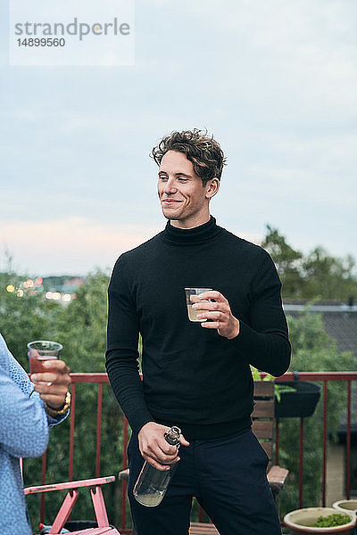 Lächelnder Mann hält Getränk in der Hand  während er einen Freund auf der Party ansieht