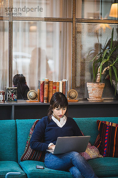 Selbstbewusste Geschäftsfrau mit Laptop auf dem Sofa im Kreativbüro