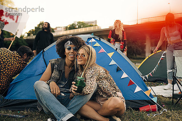 Porträt von lächelnden Freunden  die bei einer Musikveranstaltung vor dem Zelt auf dem Rasen sitzen