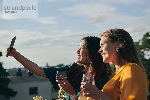 Fröhliche Freundinnen  die sich bei Sonnenschein mit dem Handy auf der Terrasse vergnügen