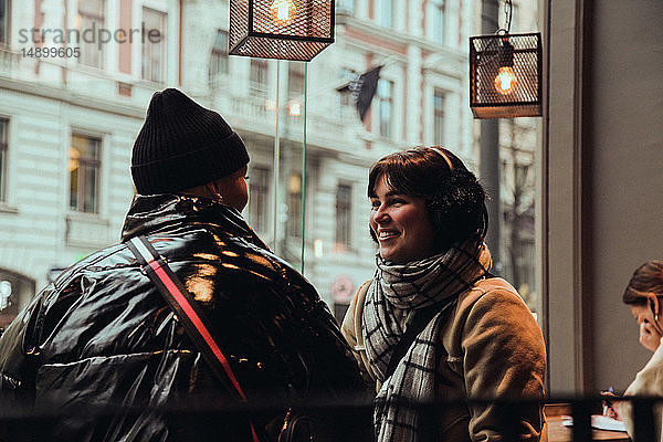 Lächelnde Freundinnen unterhalten sich  während sie im Winter im Café sitzen