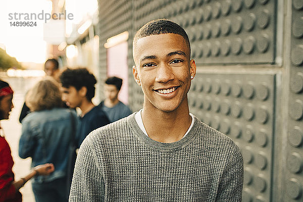 Porträt eines lächelnden Teenagers mit Freunden im Hintergrund auf der Straße