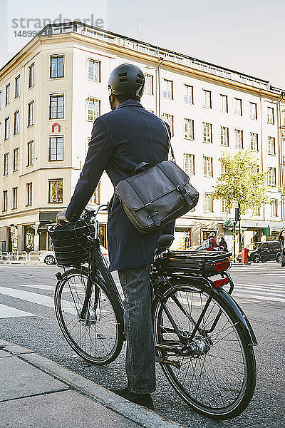 Rückansicht eines männlichen Pendlers mit einem Elektrofahrrad auf einer Straße in der Stadt