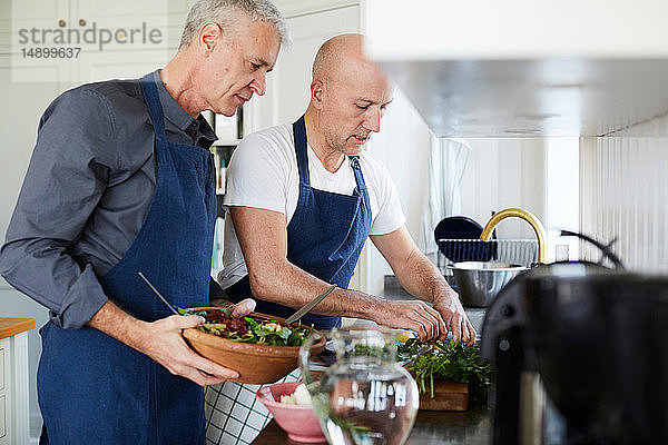 Reife Männer unterhalten sich beim Kochen in der heimischen Küche