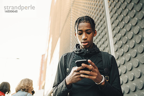 Niedriger Blickwinkel eines Teenagers  der ein Mobiltelefon benutzt  während er in der Stadt steht